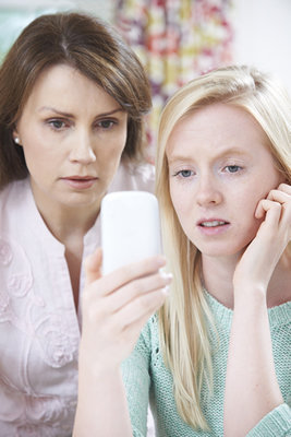 A mother and daughter looking at a phone looking shocked.